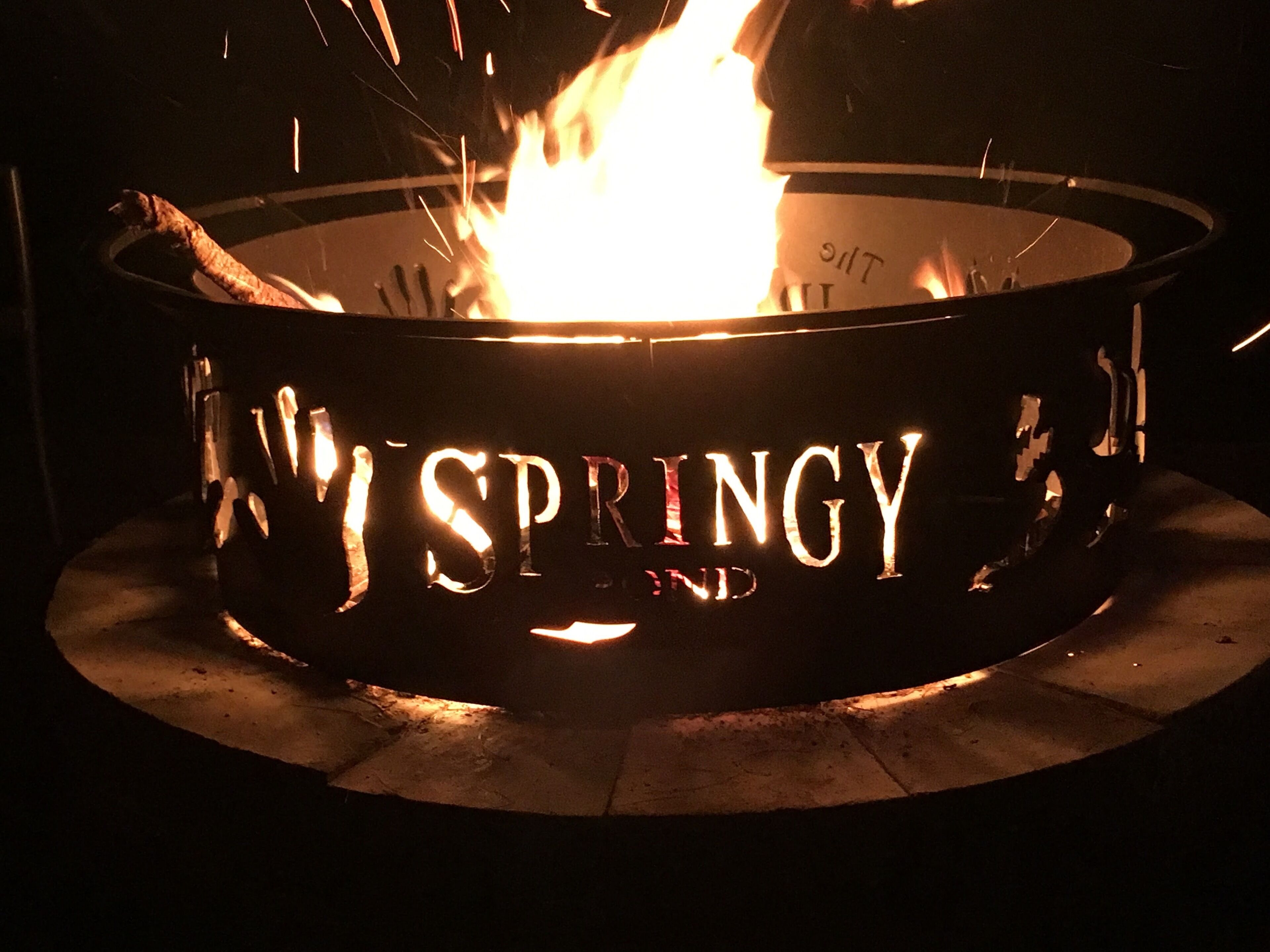 Ein metallischer Feuerkorb mit dem Schriftzug „SPRINGY“, eingebettet in eine kreisförmige Steinsockel.