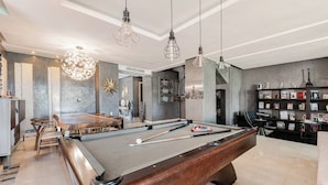 A modern pool table in a spacious room with a dining area, bookshelves, and a cityscape view.