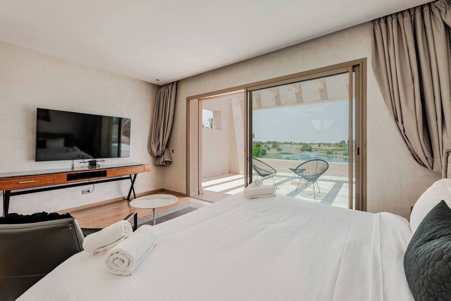 Ein Hotelzimmer mit Bett, Fernseher, Schreibtisch und einem Balkon mit Sitzgelegenheiten.