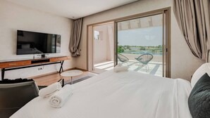 A hotel room with a bed, a TV, a desk, and a balcony with chairs.