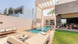 A modern outdoor pool area with lounge chairs, a small table, and a covered seating area.