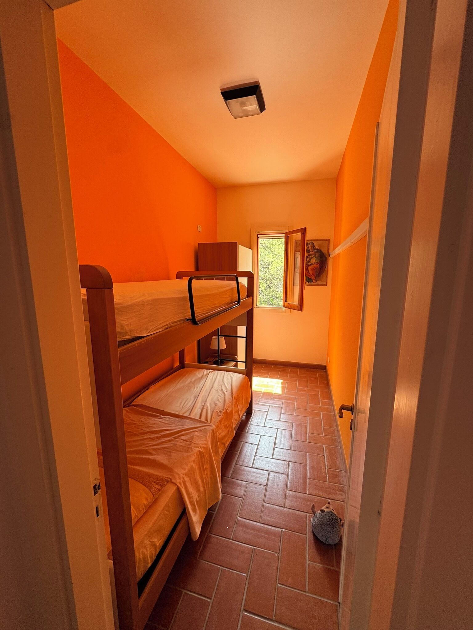 Ein Schlafsaalzimmer mit zwei Etagenbetten, einem Fenster mit Blick auf Grünflächen und einem Fliesenboden.