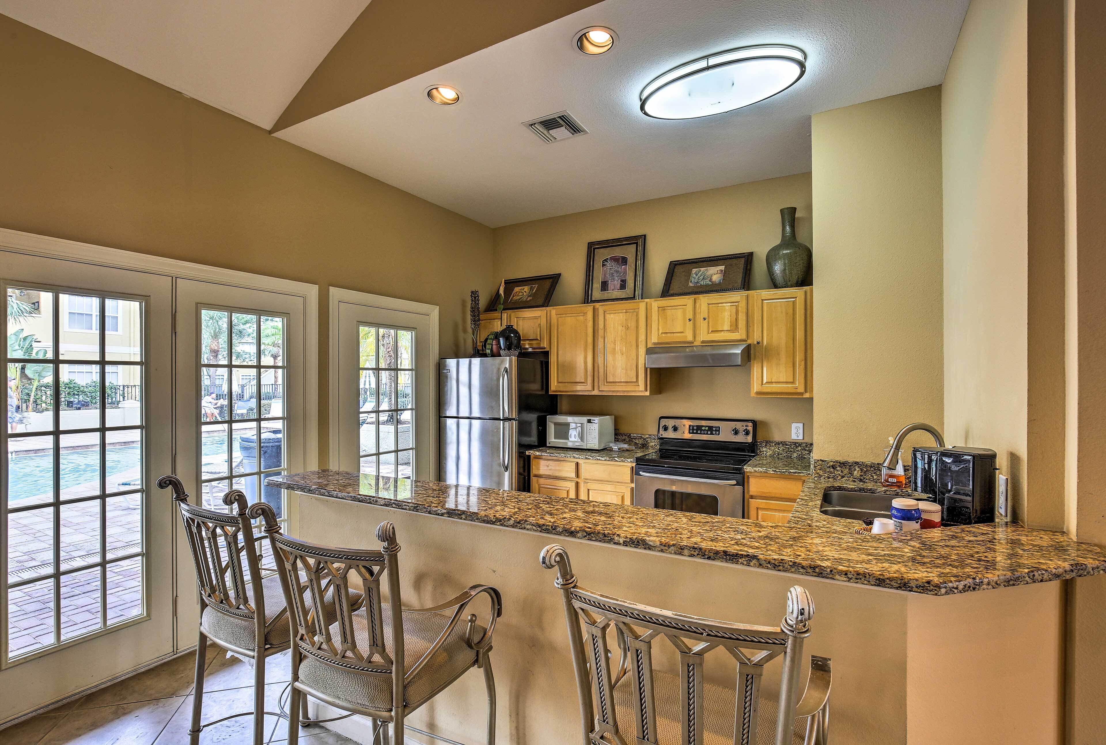 A kitchen with granite countertops, wooden cabinets, stainless steel appliances, and a bar area with metal chairs.