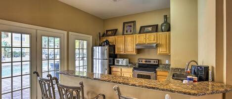 A kitchen with granite countertops, wooden cabinets, stainless steel appliances, and a bar area with metal chairs.