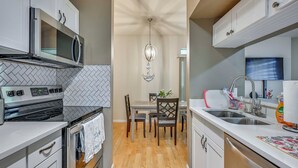 Een kleine keuken met een magnetron, fornuis, oven en spoelbak. Er staat een eettafel met stoelen en erboven een kroonluchter.