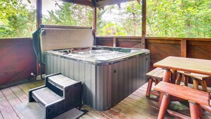 Un jacuzzi con escalones, una mesa de madera y un banco en una terraza de madera con vistas a árboles.