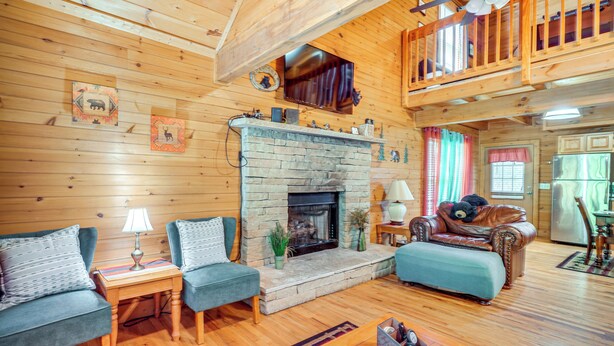 Interior acogedor de una cabaña con chimenea de piedra, paredes de madera y un altillo.