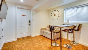 Una habitación con un sofá, una mesa con dos sillas, un reloj en la pared y una puerta con un letrero.
