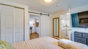 Un dormitorio con una cama, una mesita de noche, un aparador y un baño visible a través de una puerta abierta.