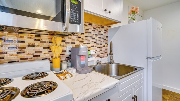 Una cocina moderna con estufa blanca, microondas, cafetera y un lavamanos de acero inoxidable.