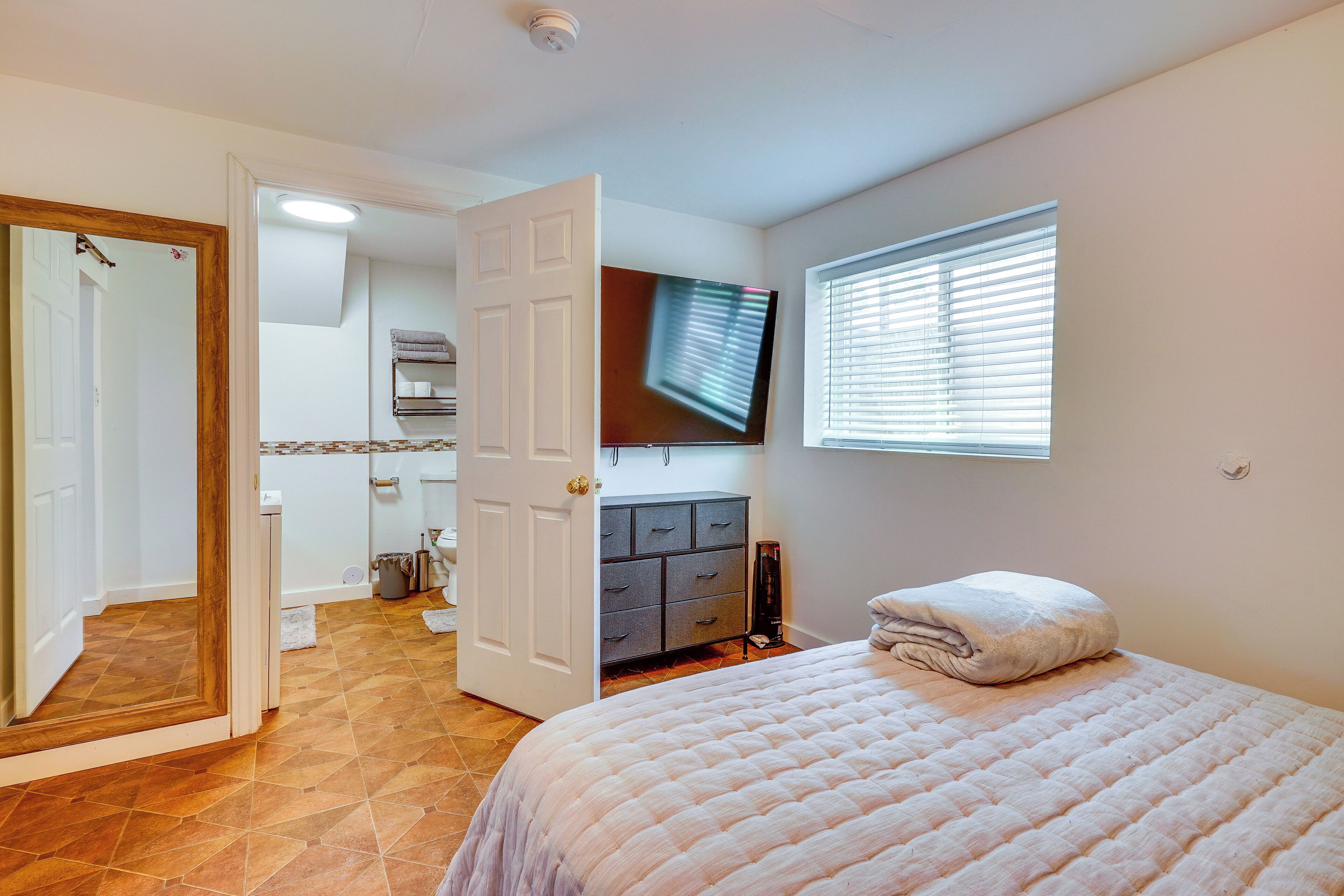 A bedroom with a bed, a television, a dresser, and a door leading to another room.