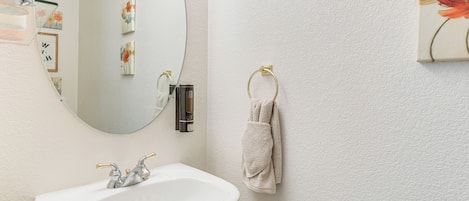 A bathroom with a white sink, a mirror, and a towel ring on the wall.