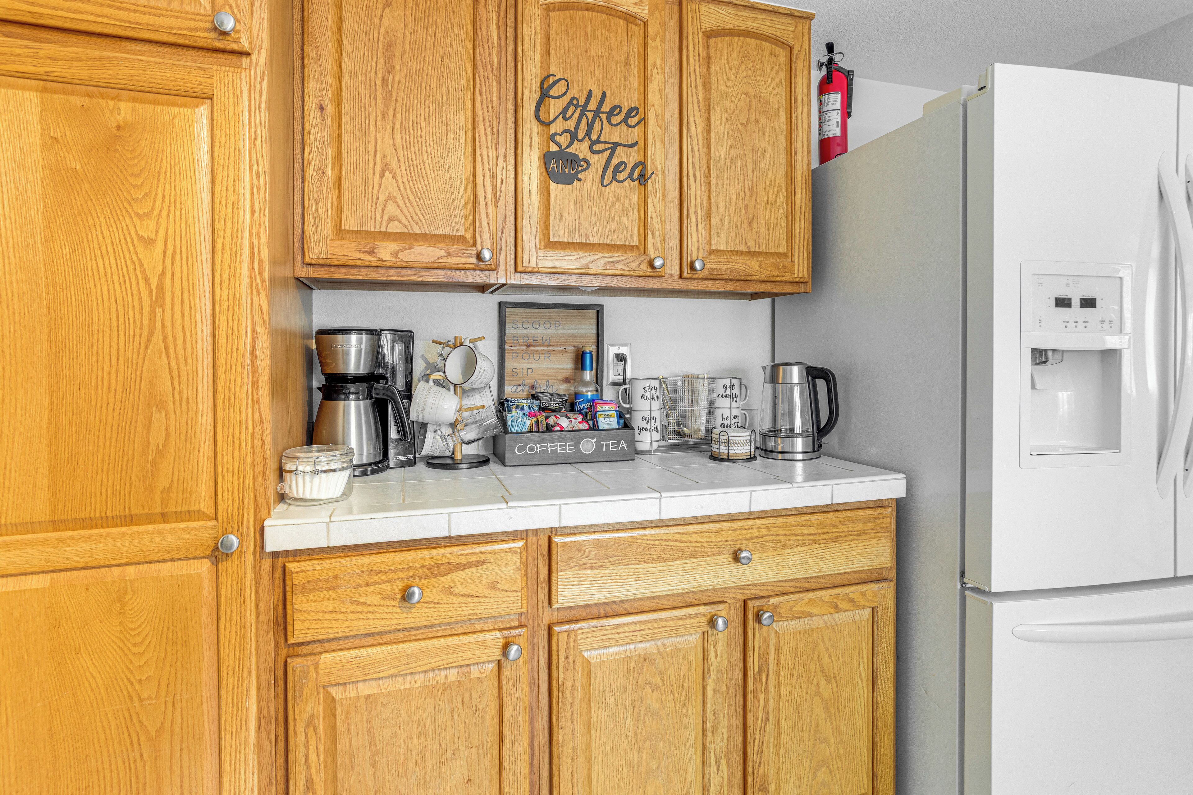 Una cocina con gabinetes de madera, una cafetera, un hervidor y un refrigerador blanco.