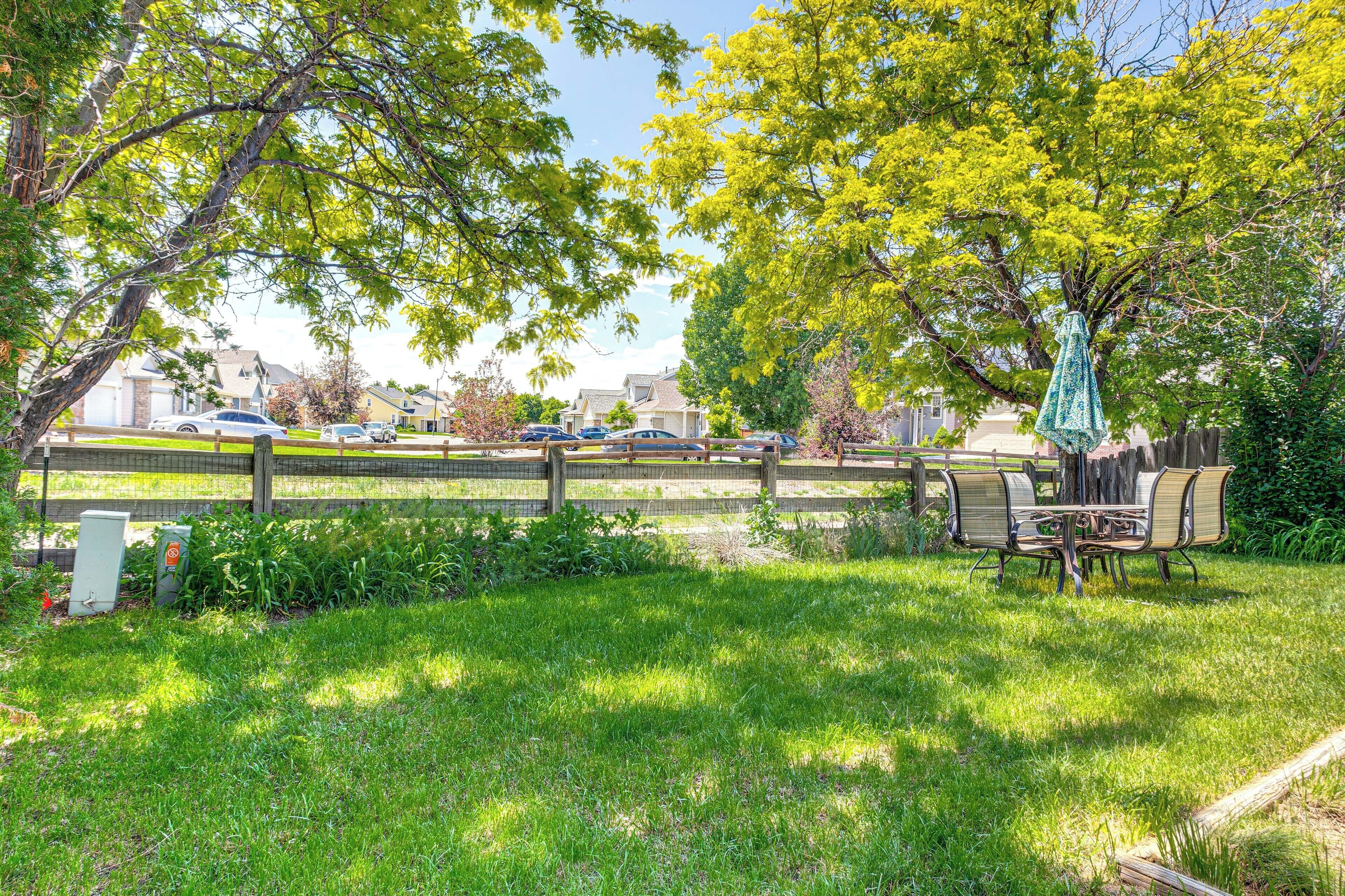 A grassy outdoor area with a wooden fence, a picnic table, and chairs.