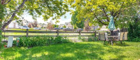A grassy outdoor area with a wooden fence, a picnic table, and chairs.
