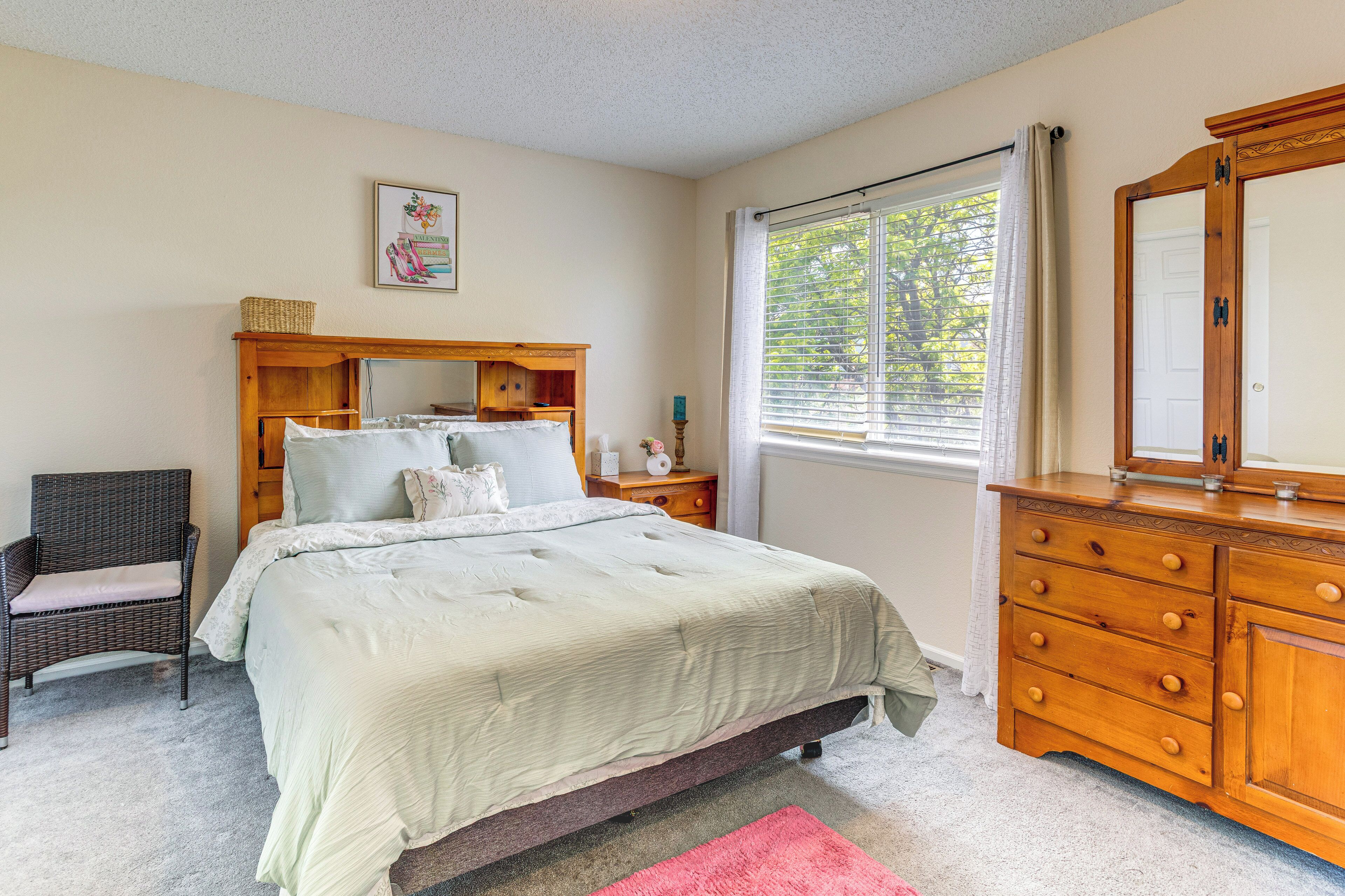 A bedroom with a bed, dresser, chair, and a window with blinds.