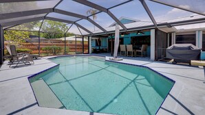 A covered swimming pool with a clear blue water, surrounded by a metal frame structure, and equipped with lounge chairs and a barbecue area.