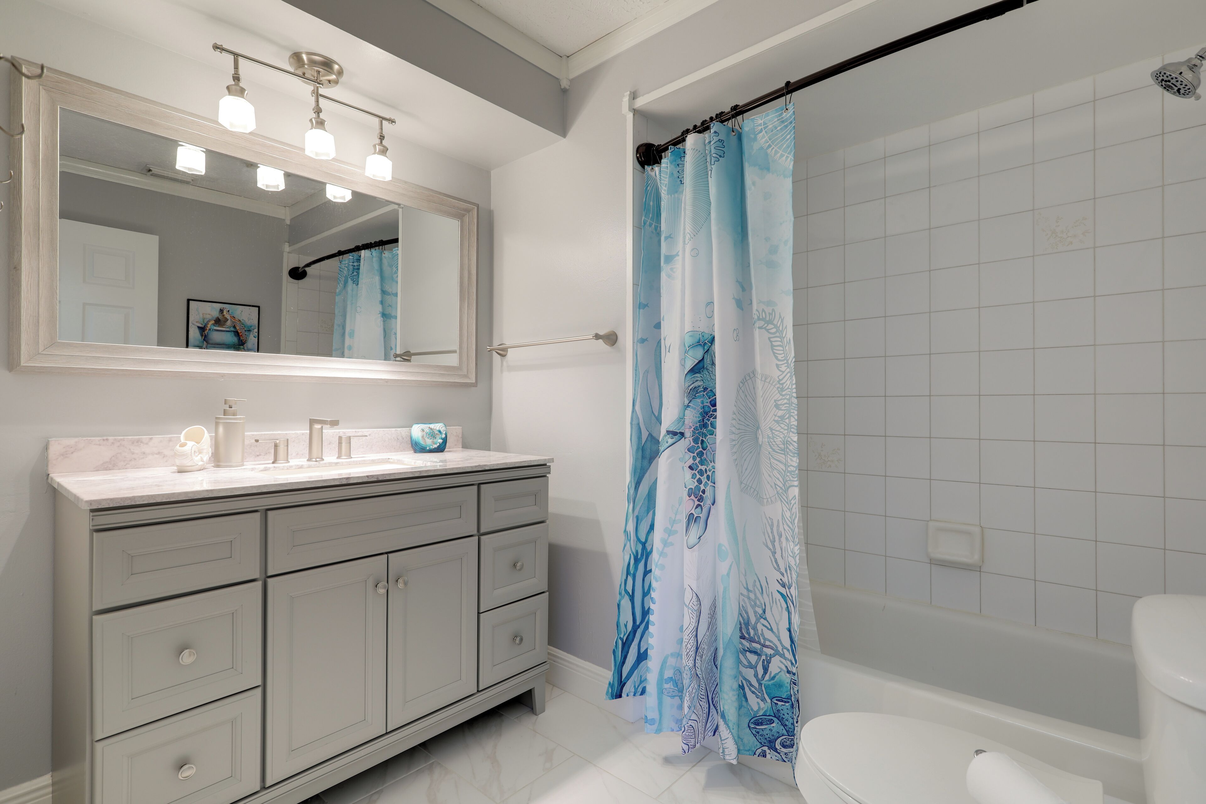 Un baño con tocador, un espejo grande, cortina de ducha con diseño marino y un inodoro.