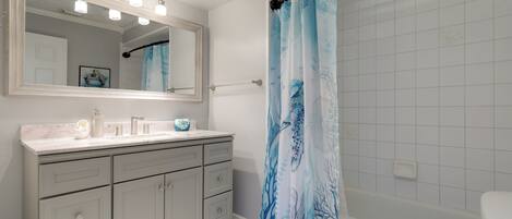 Un baño con tocador, un espejo grande, cortina de ducha con diseño marino y un inodoro.