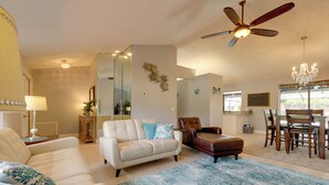 A spacious living room with a white sofa, a brown leather chair, and a dining area with a wooden table and chairs.