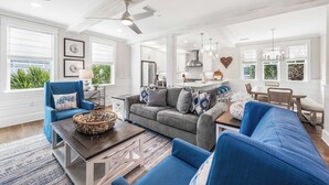 Un salón espacioso con un sofá gris, sillones azules y una zona de comedor con mesa y sillas de madera.