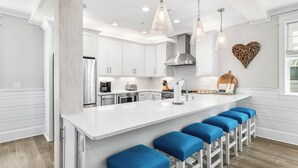Cocina moderna con armarios blancos, una isla central con taburetes de bar, iluminación colgante y una decoración de pared con forma de corazón.