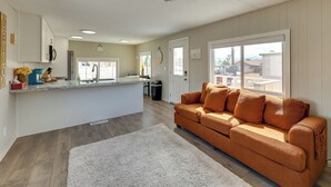 A modern living room with a sofa, a kitchen area, and a large window. - Riverfront Bullhead City Home, Near Casinos (Bullhead City)