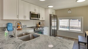 A modern kitchen with white cabinets, stainless steel appliances, a granite countertop, and a large window with a city view. - Riverfront Bullhead City Home, Near Casinos (Bullhead City)