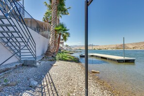 A waterfront property with a staircase leading to a balcony, a dock extending into the water, and a clear view of the surrounding landscape.