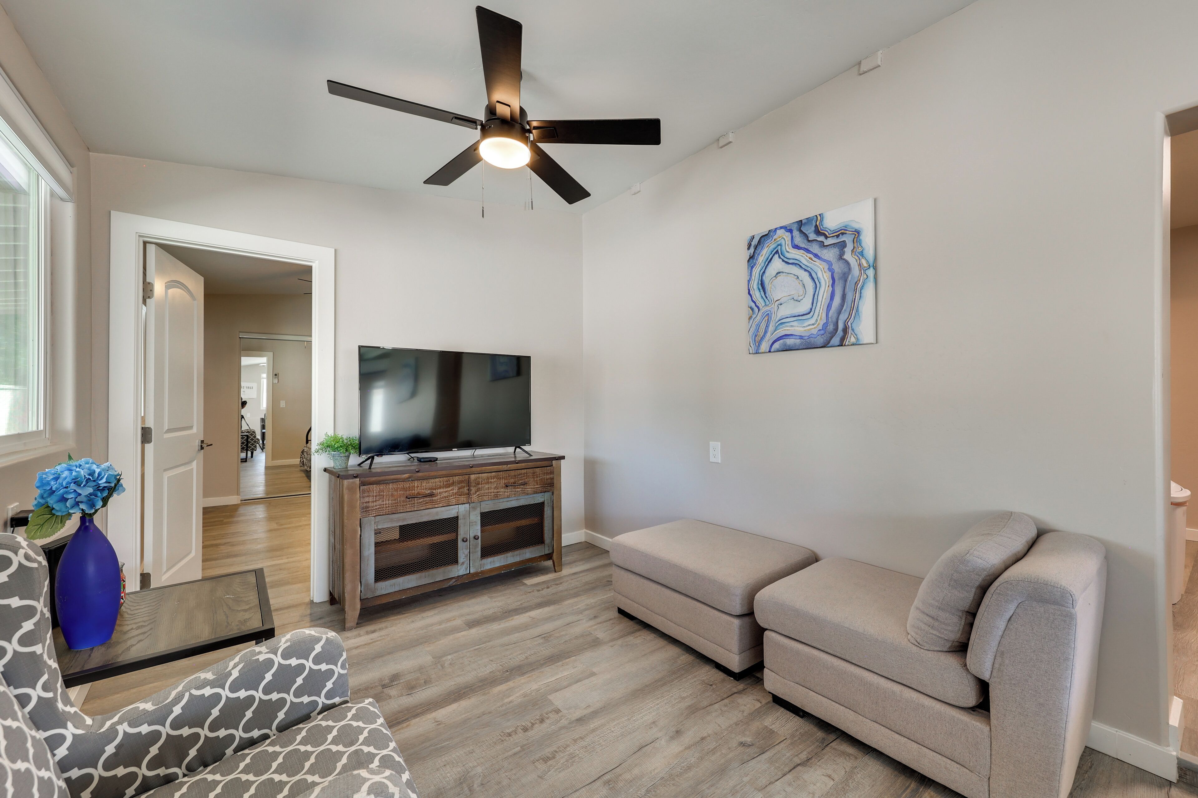 A living room with a ceiling fan, a flat-screen TV on a wooden entertainment unit, a beige sofa, and a patterned armchair.