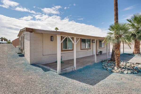 A single-story building with a covered porch, a small outdoor seating area, and a gravel driveway.