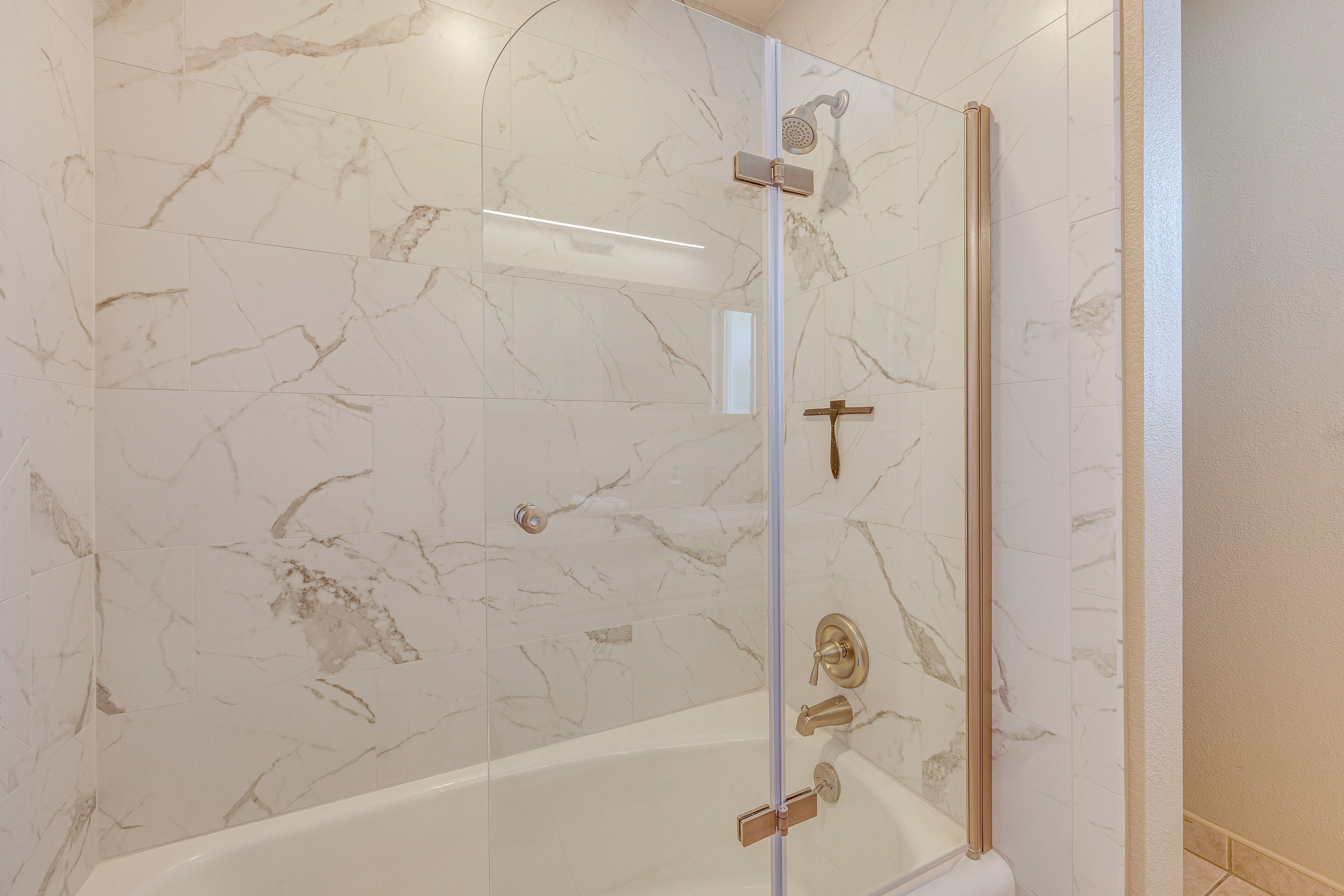 Een moderne badkamer met een douchecabine van glas, marmeren wanden en een witte badkuip.