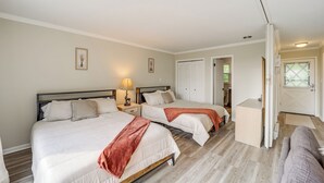 Quarto de hotel com duas camas, uma mesa pequena e uma porta que dá para outro espaço.