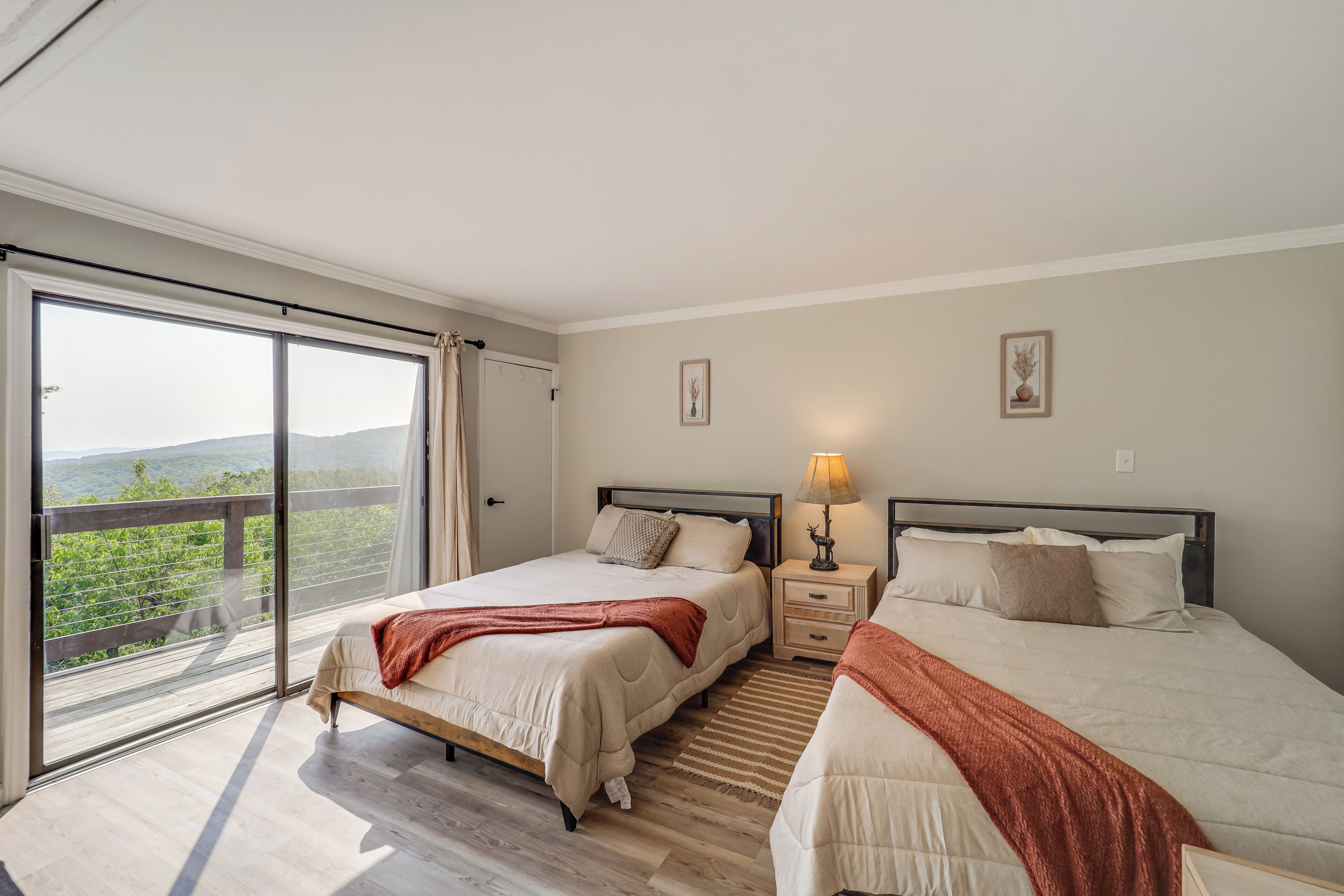 A bedroom with two beds, a large sliding glass door leading to a balcony, and a nightstand with a lamp.