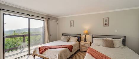 A bedroom with two beds, a large sliding glass door leading to a balcony, and a nightstand with a lamp.