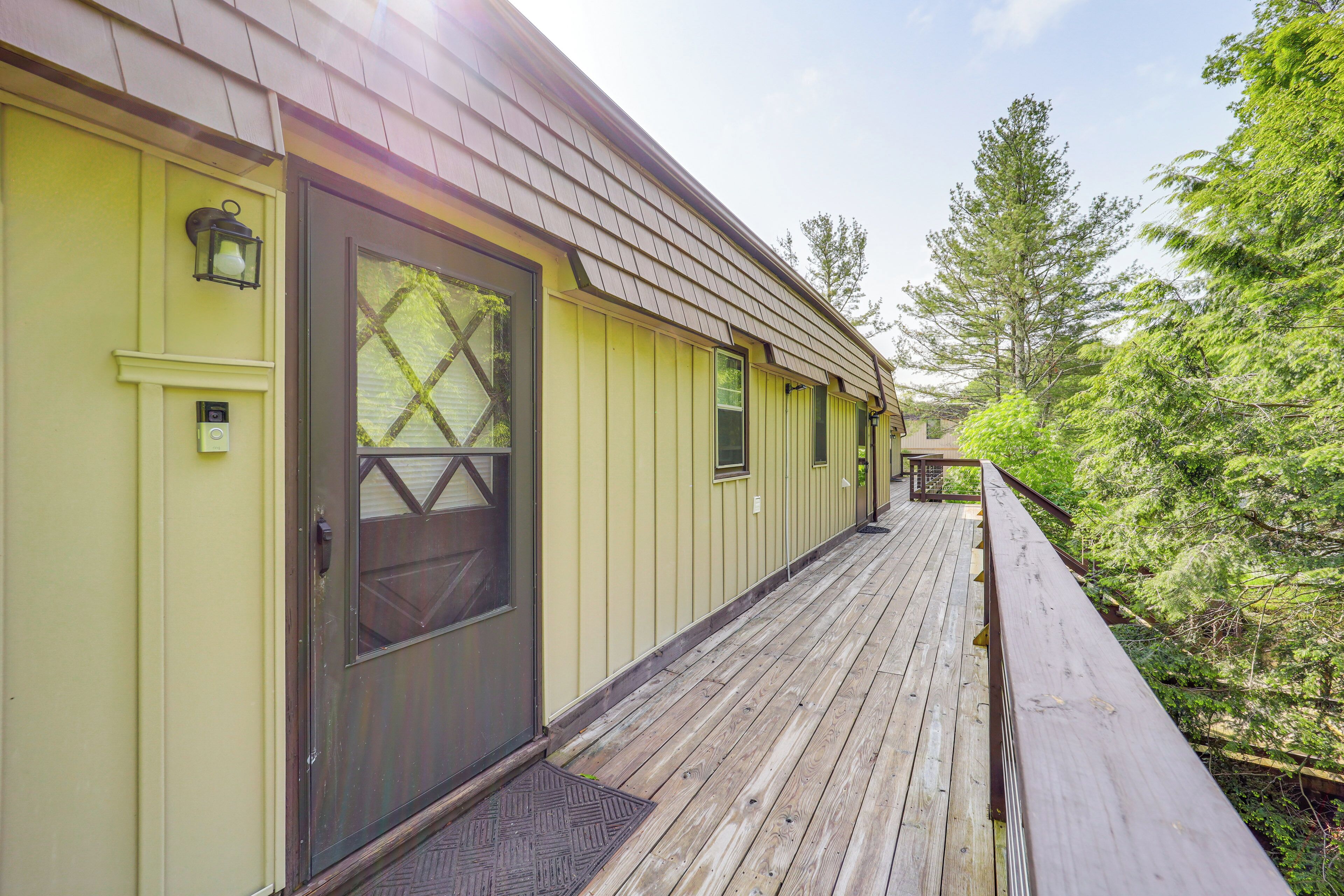 A wooden deck leading to a yellow building with a dark door and windows.