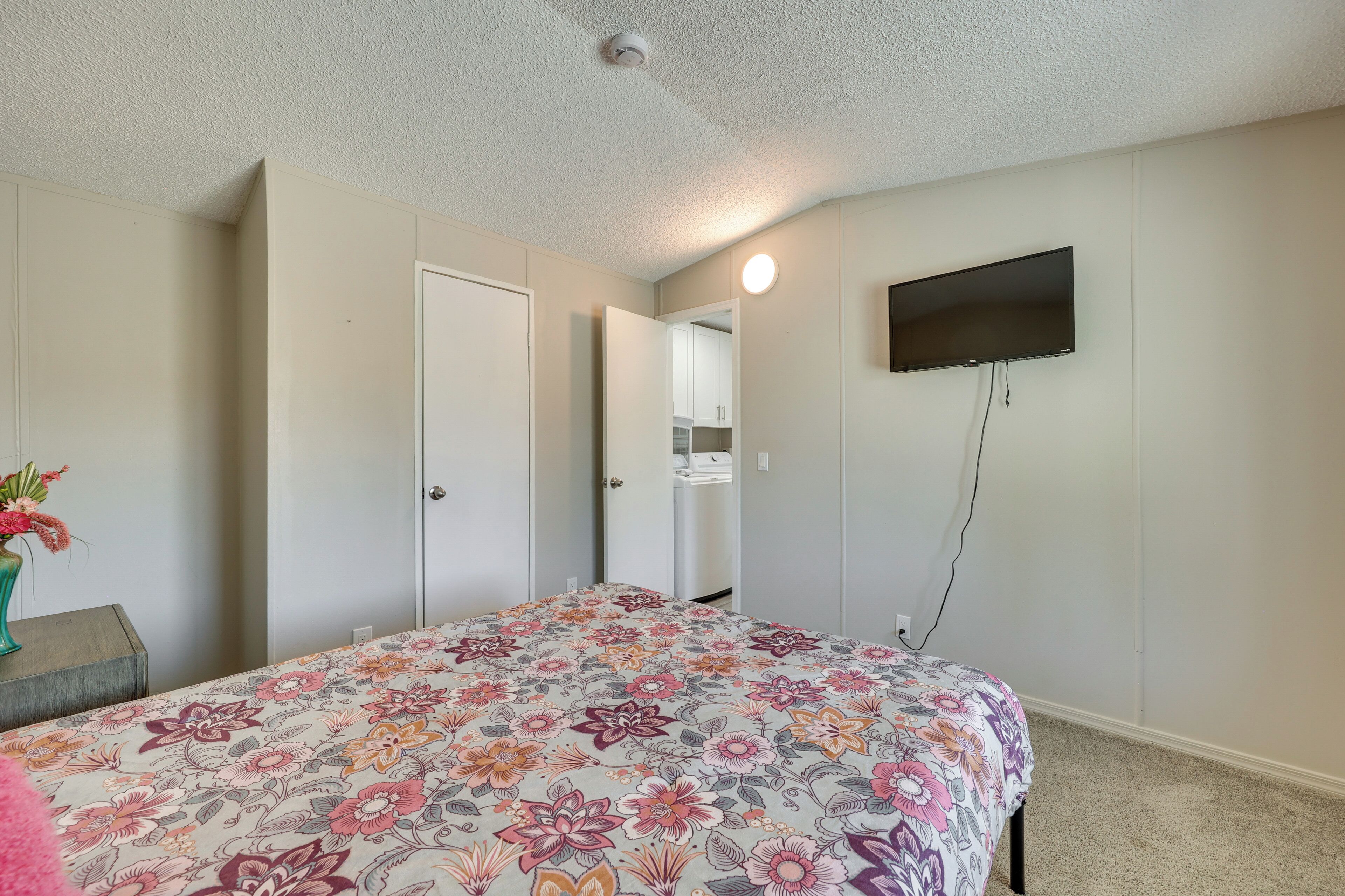 A bedroom with a floral bedspread, a flat-screen TV mounted on the wall, and a door leading to a bathroom.