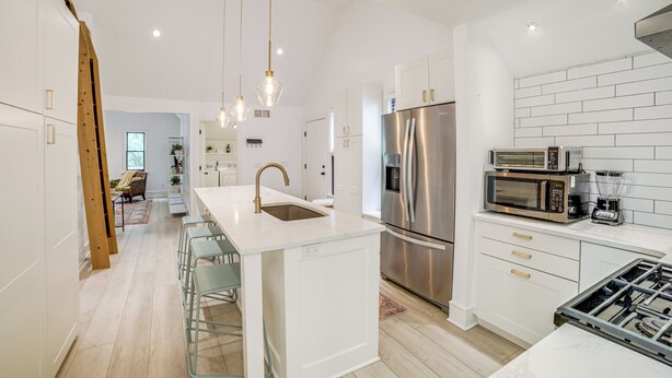Une cuisine moderne avec des meubles blancs, des appareils en acier inoxydable et un îlot central doté de tabourets de bar.