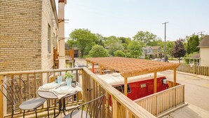 Une terrasse en bois avec une table et des chaises, un camping-car rouge et, au fond, un bâtiment en briques.