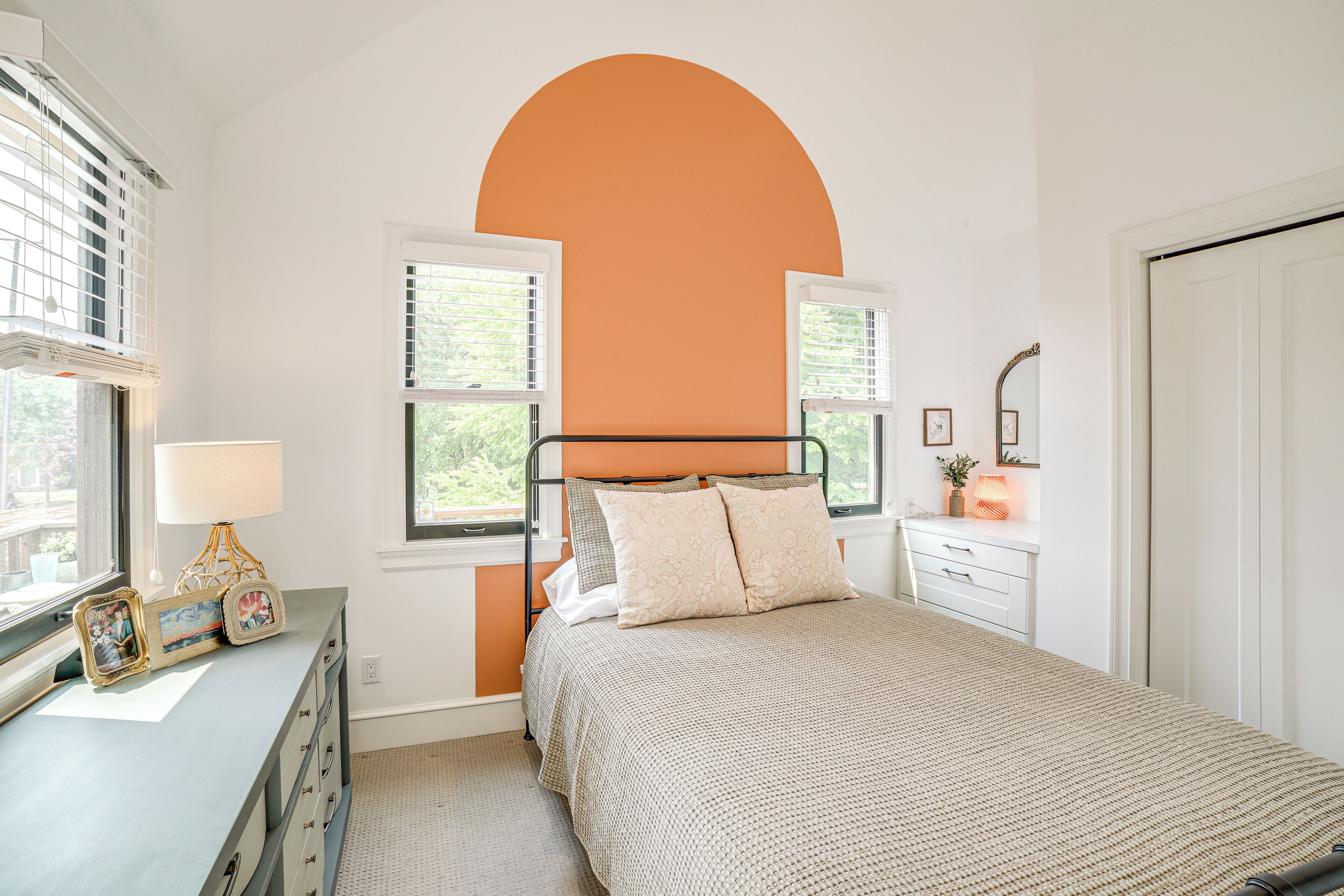 A bedroom with a bed, dresser, bedside table, lamp, and picture frames.