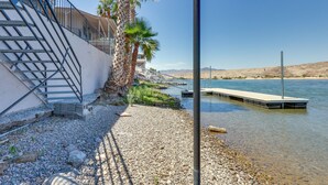 A waterfront property with a staircase leading to a balcony, a dock extending into the water, and a clear view of the surrounding landscape. - Colorado River Retreat: Bullhead City Home w/ Deck (Bullhead City)