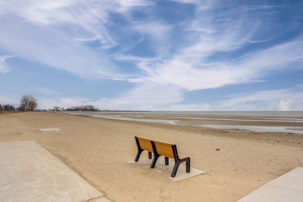 A beach with a single wooden bench and a concrete pathway. - Walk to Beach & Dtwn! Port Clinton Home (Port Clinton)