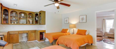 A room with two beds, a desk, and a ceiling fan.