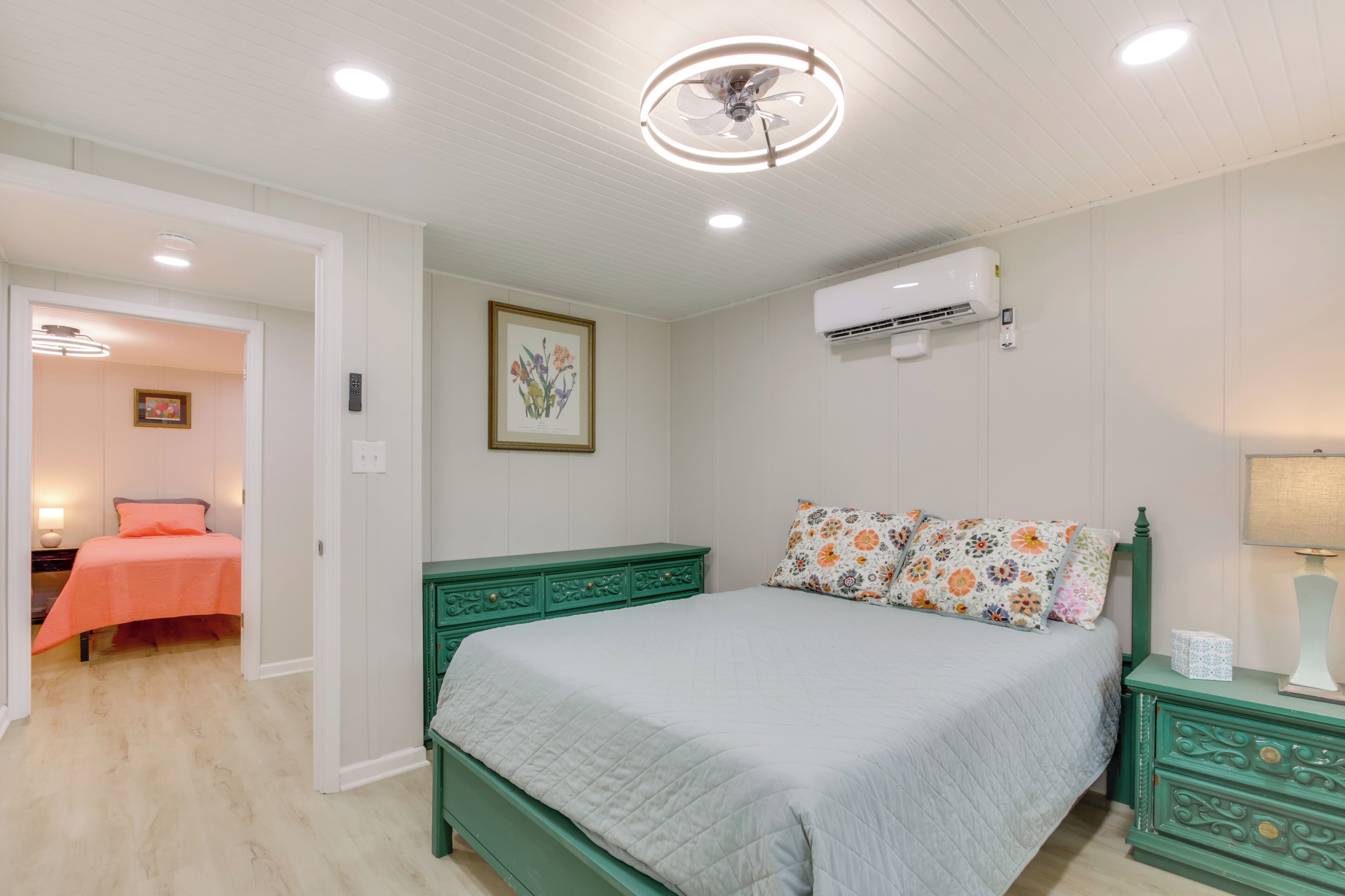 Ein Schlafzimmer mit Bett, Nachttisch, Kommode, Klimaanlage, Deckenventilator und einer Tür zu einem anderen Raum.