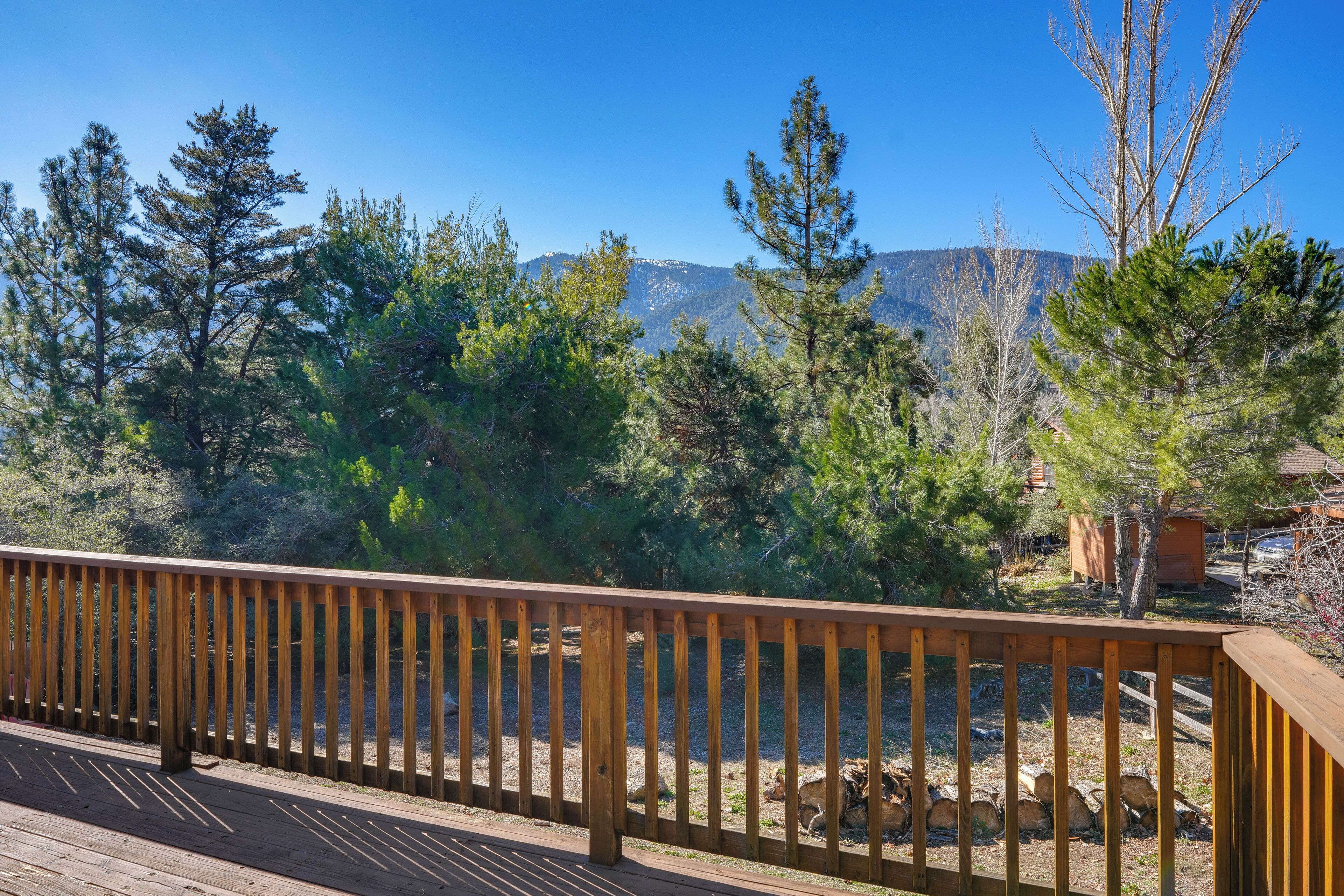 A wooden deck with a railing overlooking a natural landscape with trees and mountains.