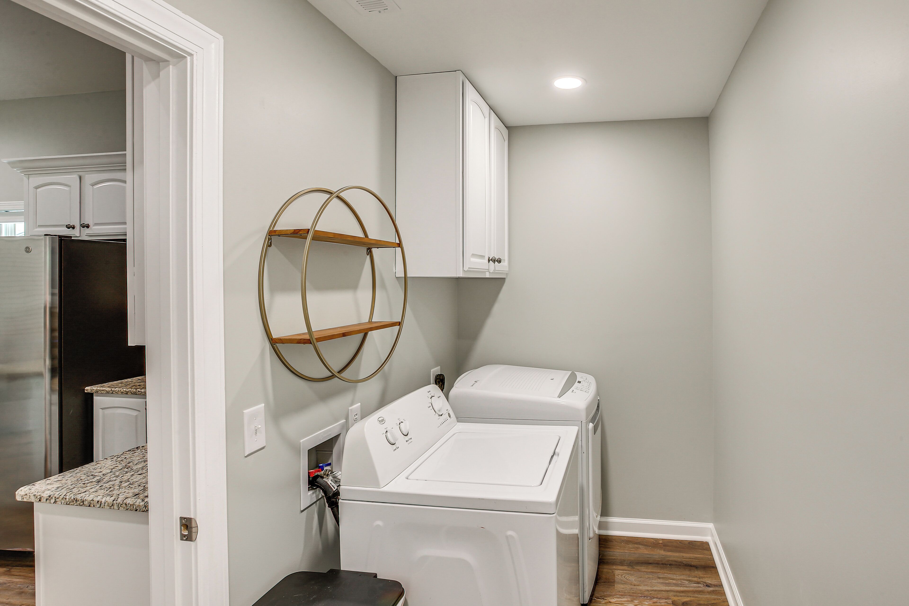 A laundry room with a washing machine and dryer, a wooden shelf, and white cabinets.