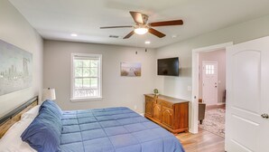 Une chambre à coucher comprenant un lit, un ventilateur de plafond, une commode, un téléviseur et une porte donnant sur une autre pièce.