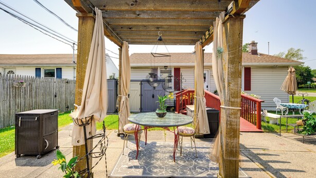 Un porche cubierto con una mesa y sillas, una pérgola de madera y una escalera roja que lleva a una casa.