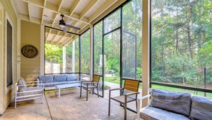 Eine überdachte Terrasse mit Sitzgelegenheiten, großen Fenstern und einem Deckenventilator.