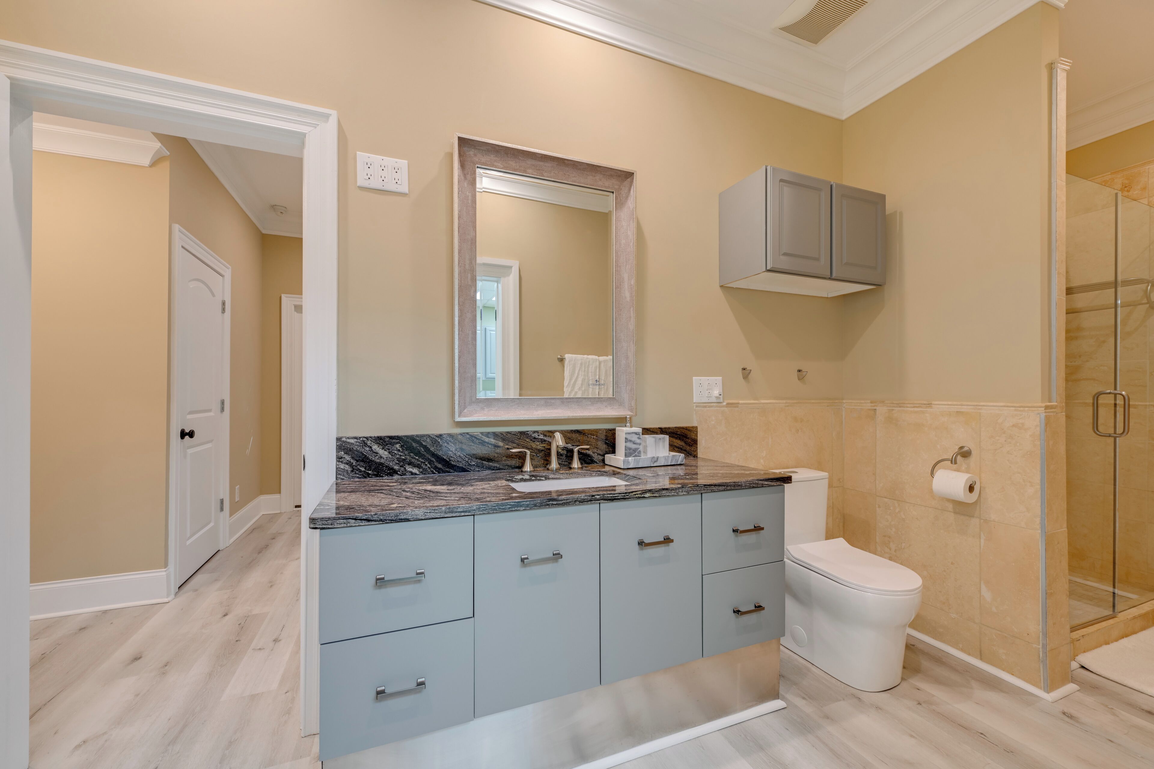A bathroom with a marble countertop, a toilet, a shower, and a cabinet above the sink.